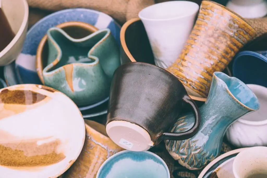 Pile of handcrafted ceramic dishes and mugs in various colors and designs. Declutter your kitchen with unique pottery.