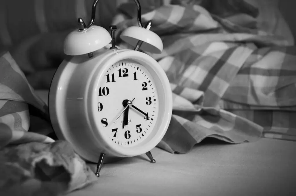 Alarm clock on a bed with a gingham sheet, reminding you to establish a bedtime routine.