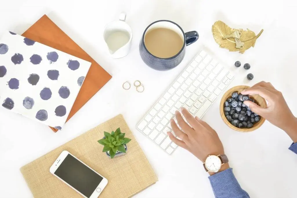 Workspace with keyboard, coffee, blueberries, phone, and notebook for blog on loving your job.