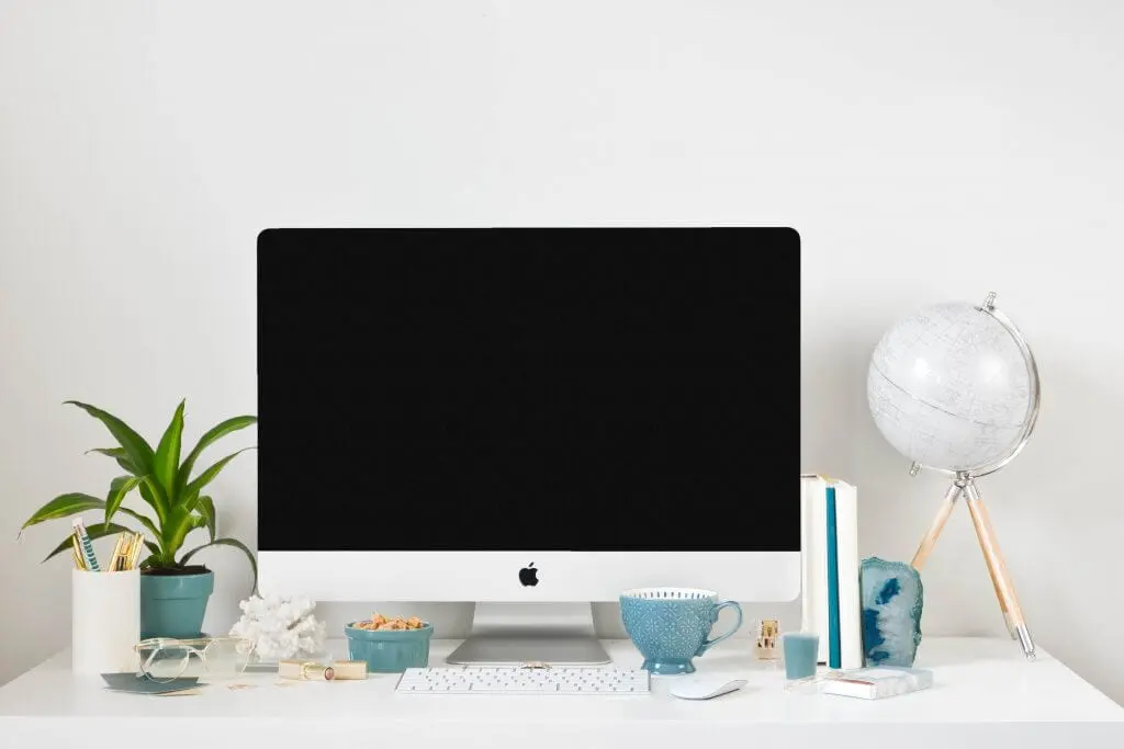 Clean white desk setup with iMac, plant, globe, and teal accents.