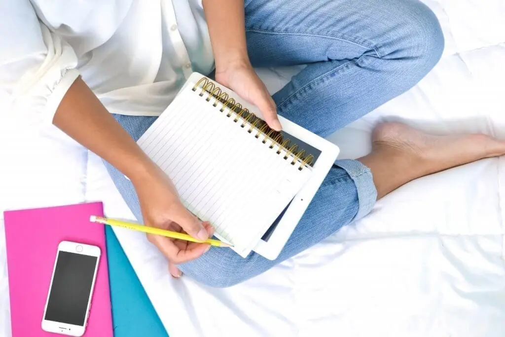 Woman in jeans sits with notebook, iPad, and phone, brainstorming how to love her job.