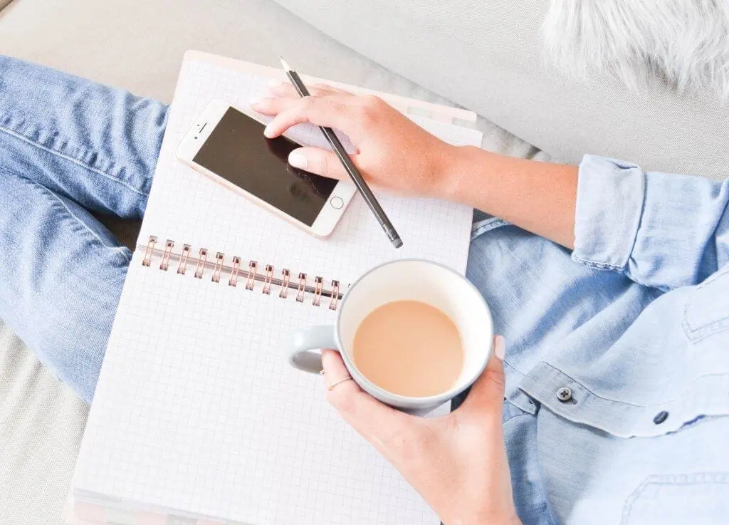 Woman with coffee, phone, and notebook planning her day.