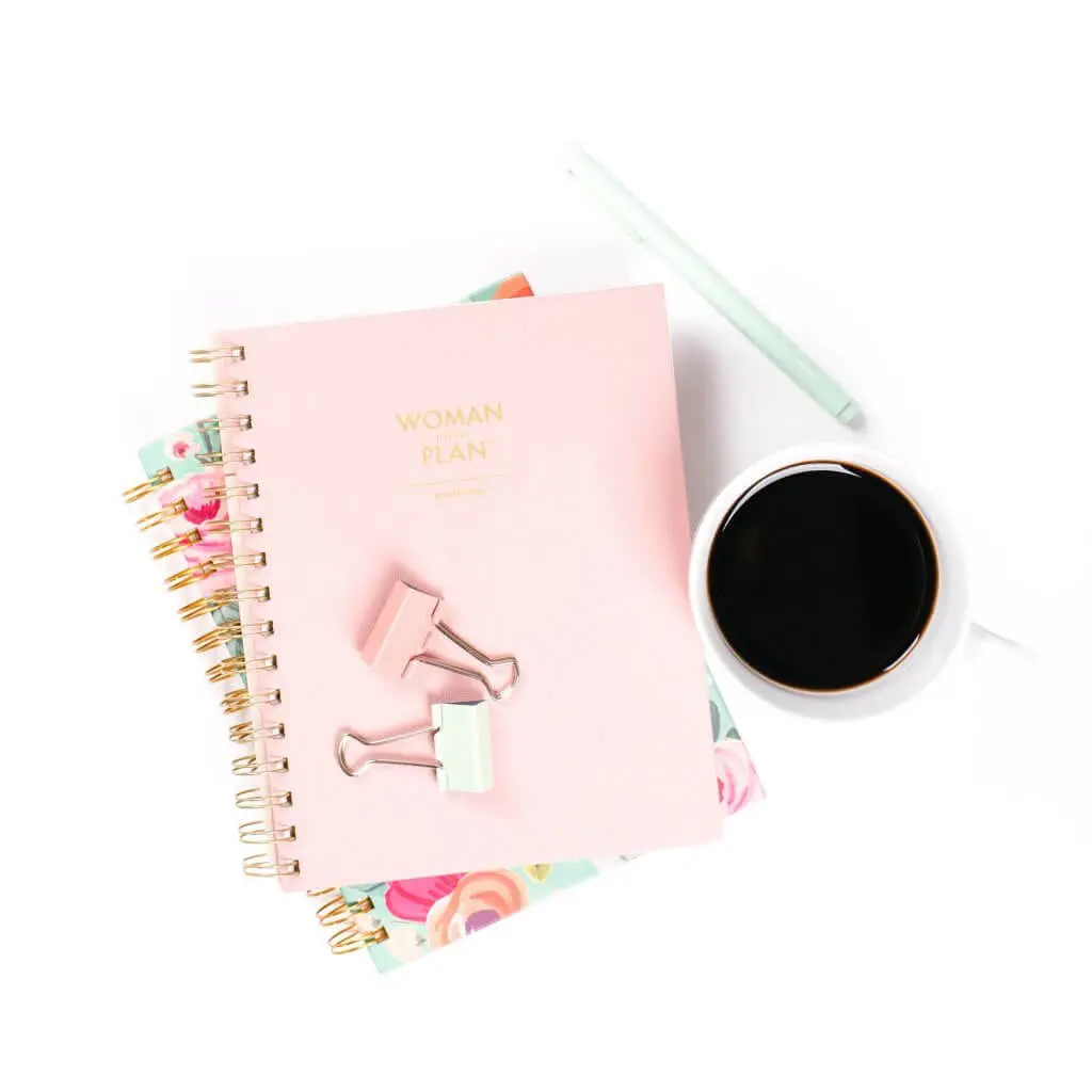 Pink "Woman with a Plan" notebook, binder clips, pen, and coffee.