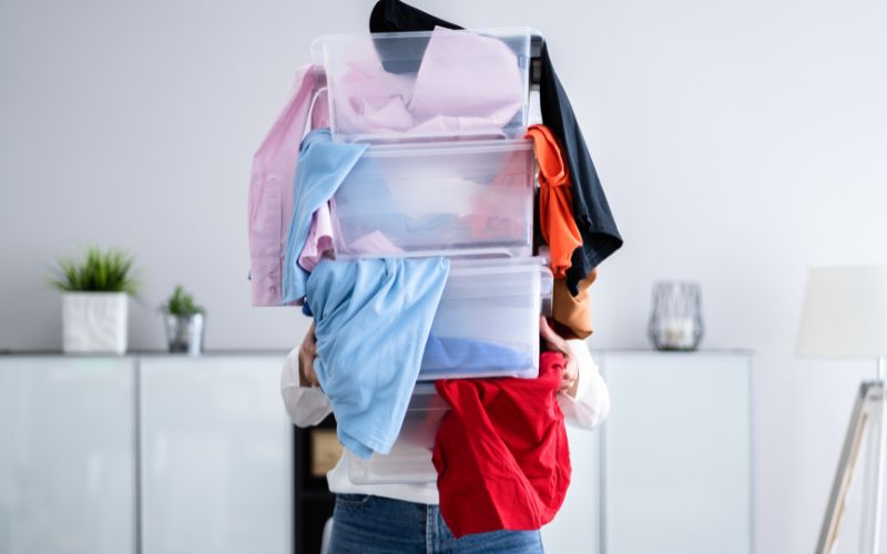 Person carrying stacked bins overflowing with colorful clothes for spring cleaning with ADHD.