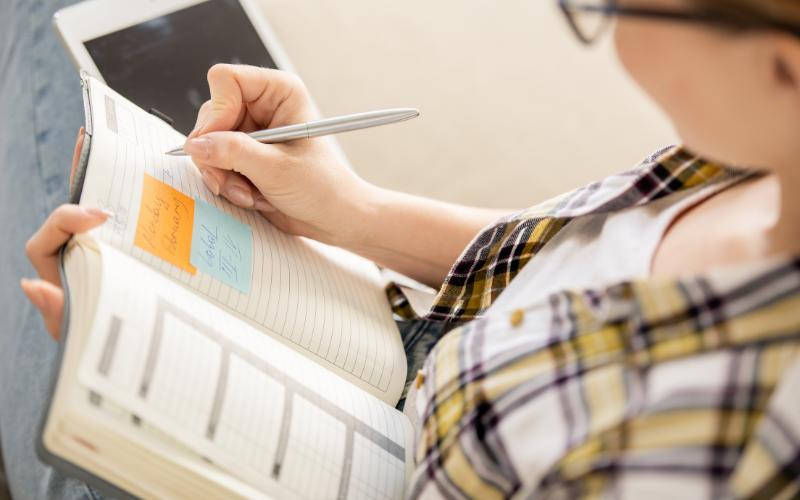 Woman writing in planner with sticky notes, planning to achieve goals with ADHD.