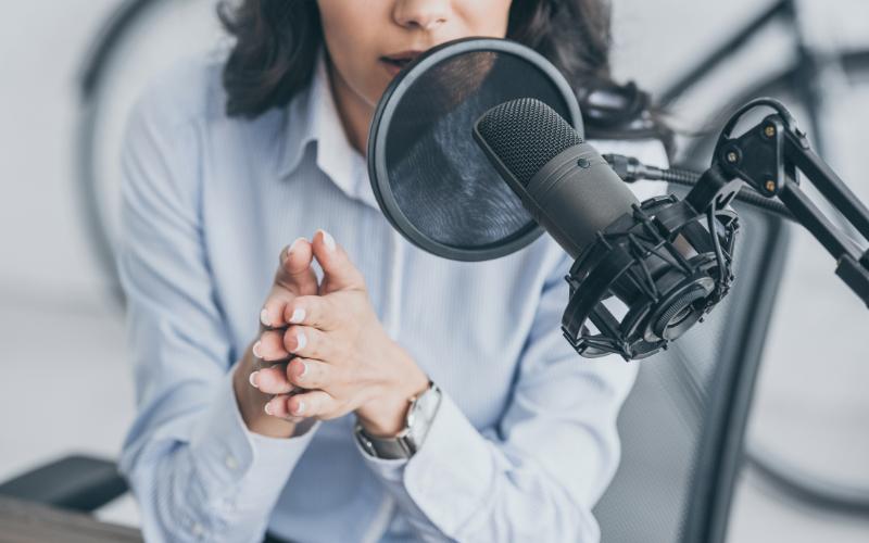 Woman recording a podcast with a microphone, celebrating 200 episodes.