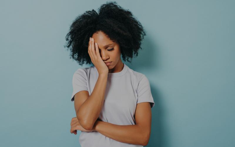 Woman with hand on forehead, looking down, indicating focus or frustration. Zoom in.