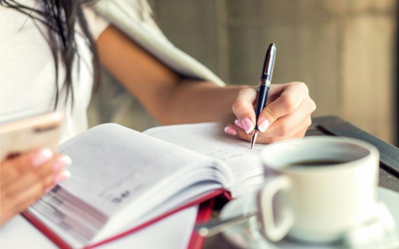Woman writing in a planner with a coffee cup; fall fresh start planning.
