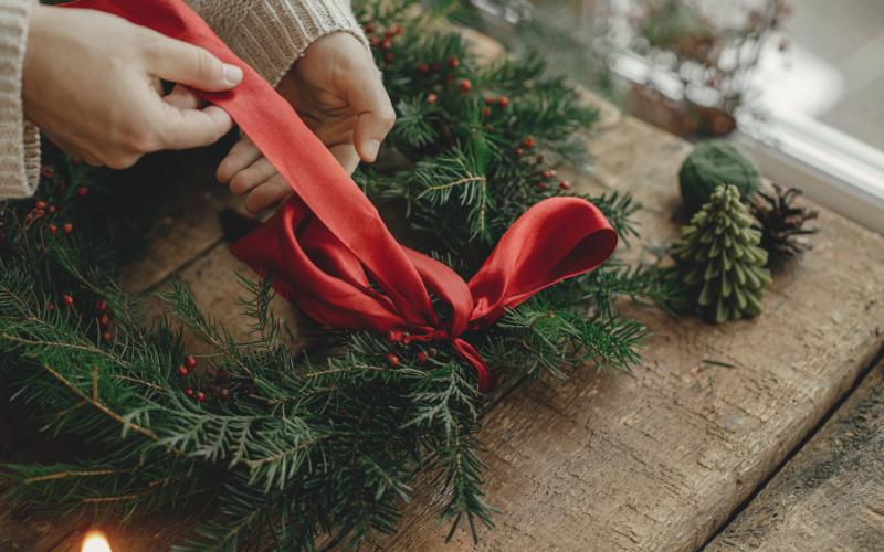 Person making a Christmas wreath with a red ribbon, simplifying ADHD holidays.