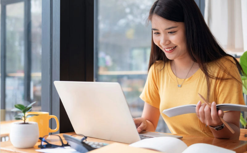 Woman smiles at laptop, notebook in hand, working to get back on track.