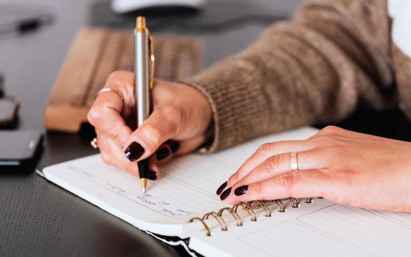 Woman writing in a notebook with a pen. Considering why am I avoiding everything.