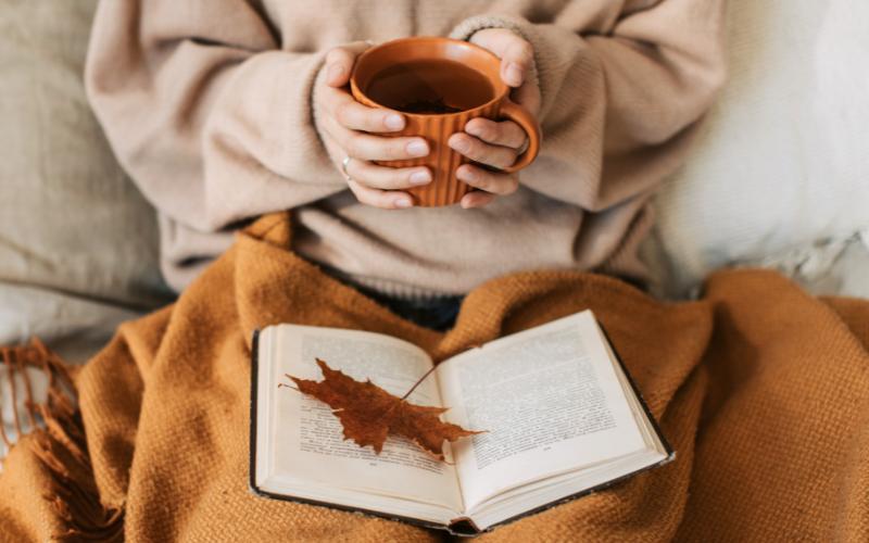 woman with tea in blanket and book