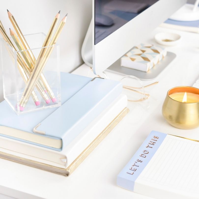 Desk with gold pencils, notebooks, candle, glasses, and a notepad that says "Let's do this.