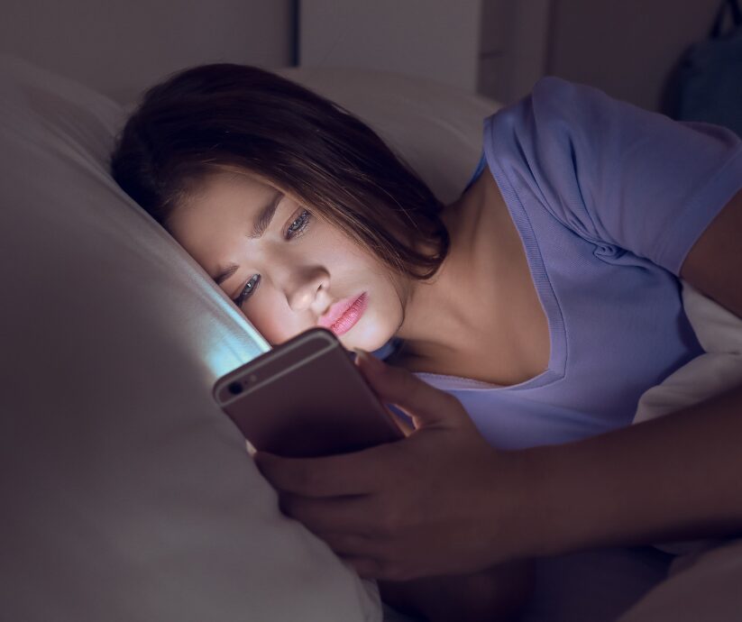 Woman awake in bed looking at her phone. ADHD sleep tips for disrupted routines.