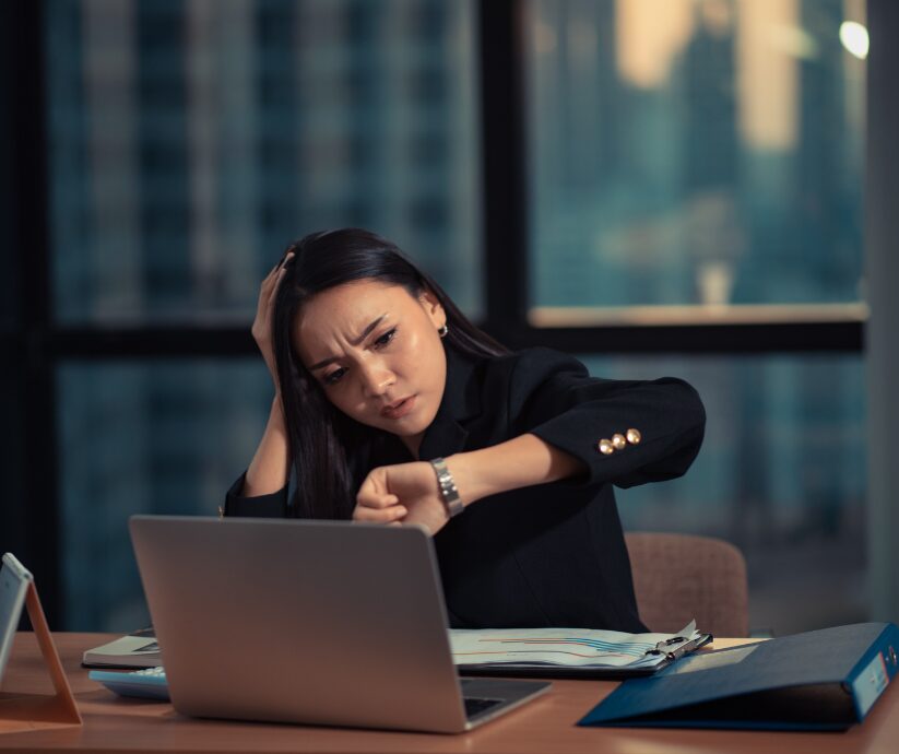 Stressed woman with high achieving ADHD checking her watch at her desk.